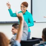 Professor smiling, students hands raised