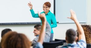 Professor smiling, students hands raised