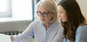 Two female professors, one older and one younger, review material on a computer screen