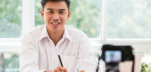 An Asian American male teacher records himself with a digital camera