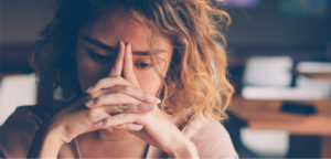 Close-up of a sad female student with hands clasped in front of her face