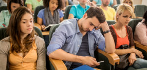 A group of disengaged college students, one of whom is idly checking his smartphone