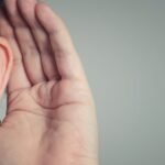 Close-up of a woman's hand cupping her ear