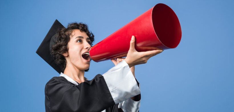 Stock photo of female student in graduation gown speaking into an old-timey megaphone