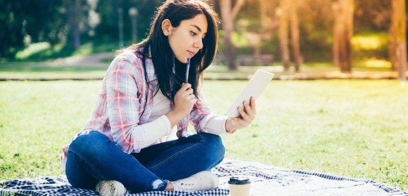 A student sitting cross-legged on a picnic blanket reads a letter on her smartphone